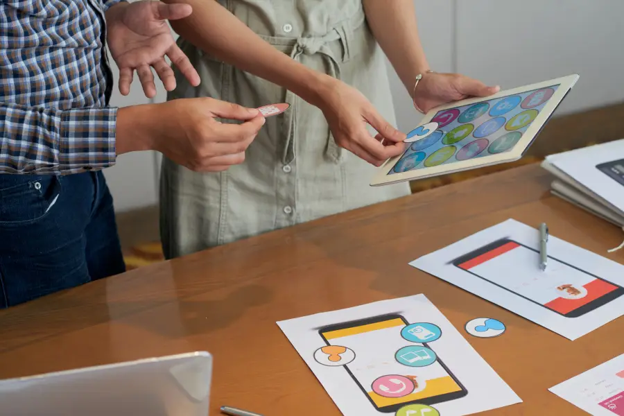 Illustration of unrecognizable colleagues looking at a tablet and trying different icons, symbolizing efforts to enhance user experience, aligned with the subtitle 'Better User Experience, touchvision.site