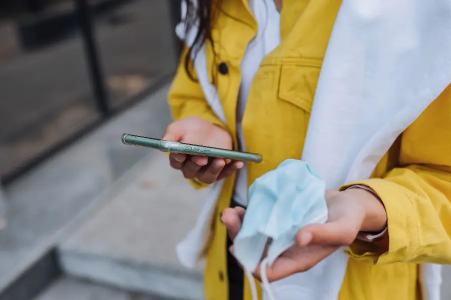 Illustration of a woman holding a smartphone and wearing a mask, navigating on her phone, representing user-friendly navigation, aligned with the article 'User-Friendly Navigation, touchvision.site